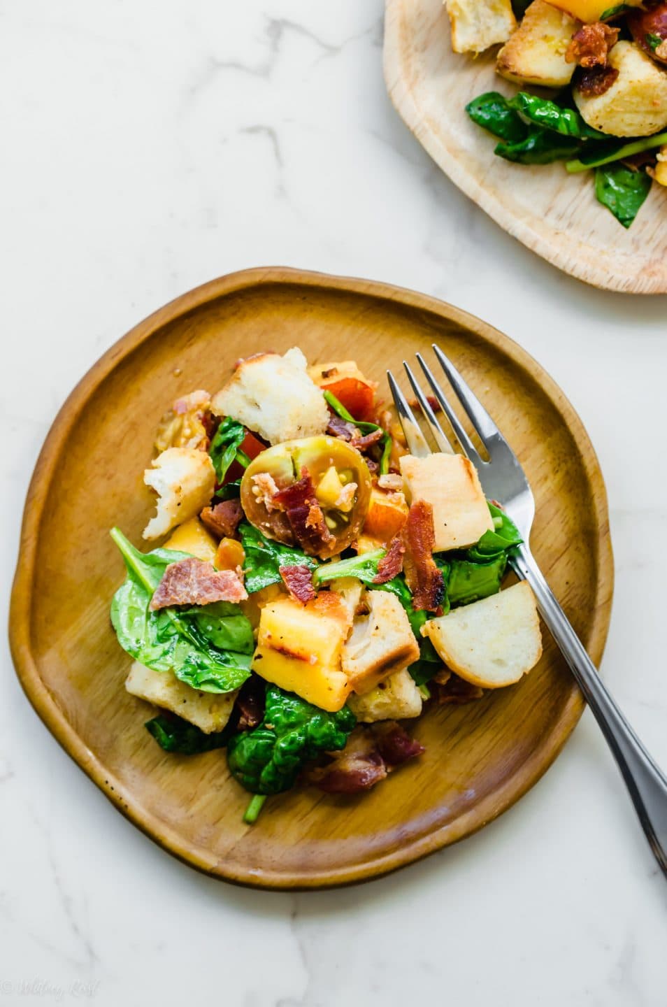 A wooden plate and silver fork with a serving of BLT Panzanella Salad.