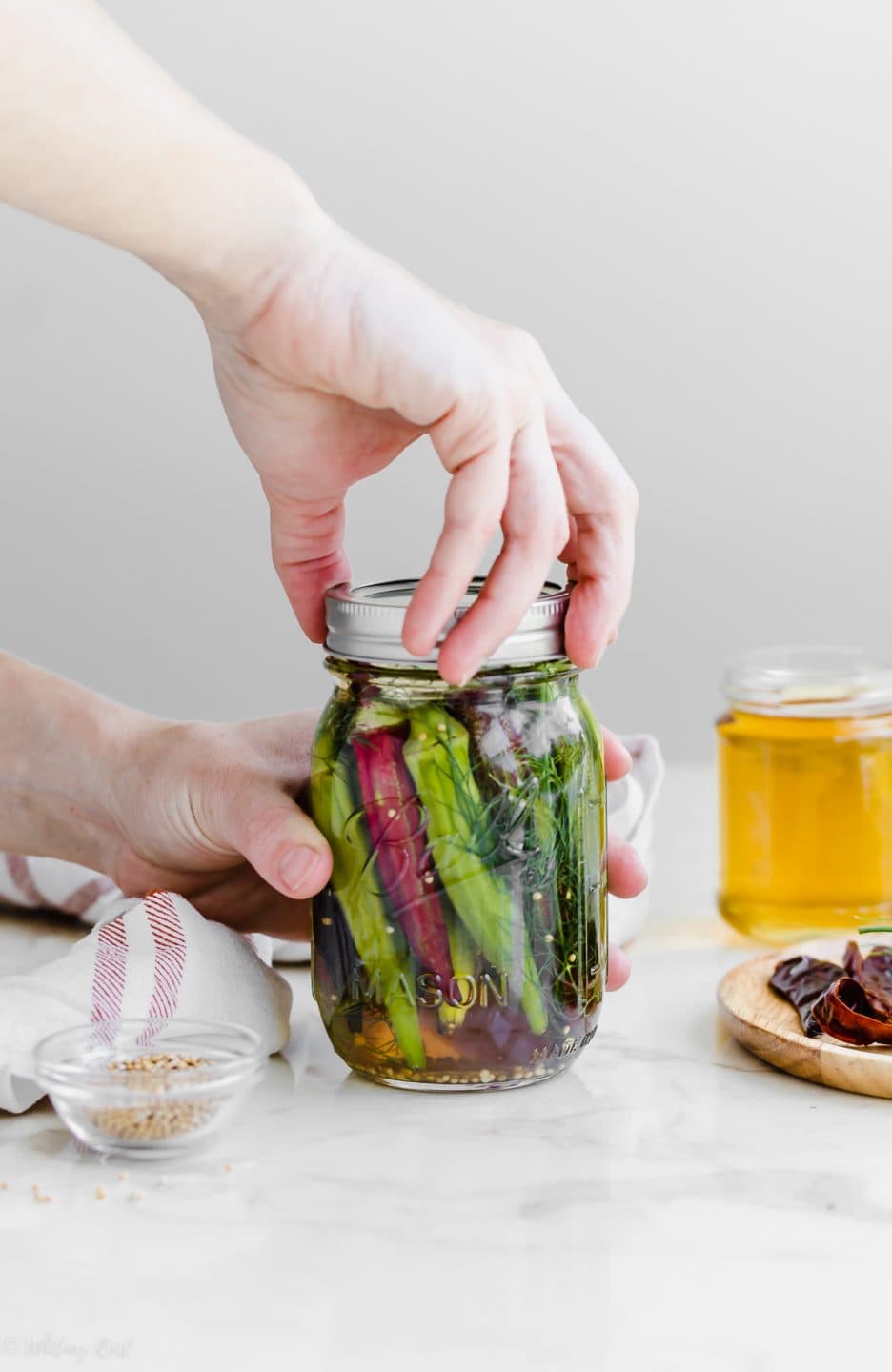 A hand placing the ring on a canning jar of pickled okra.
