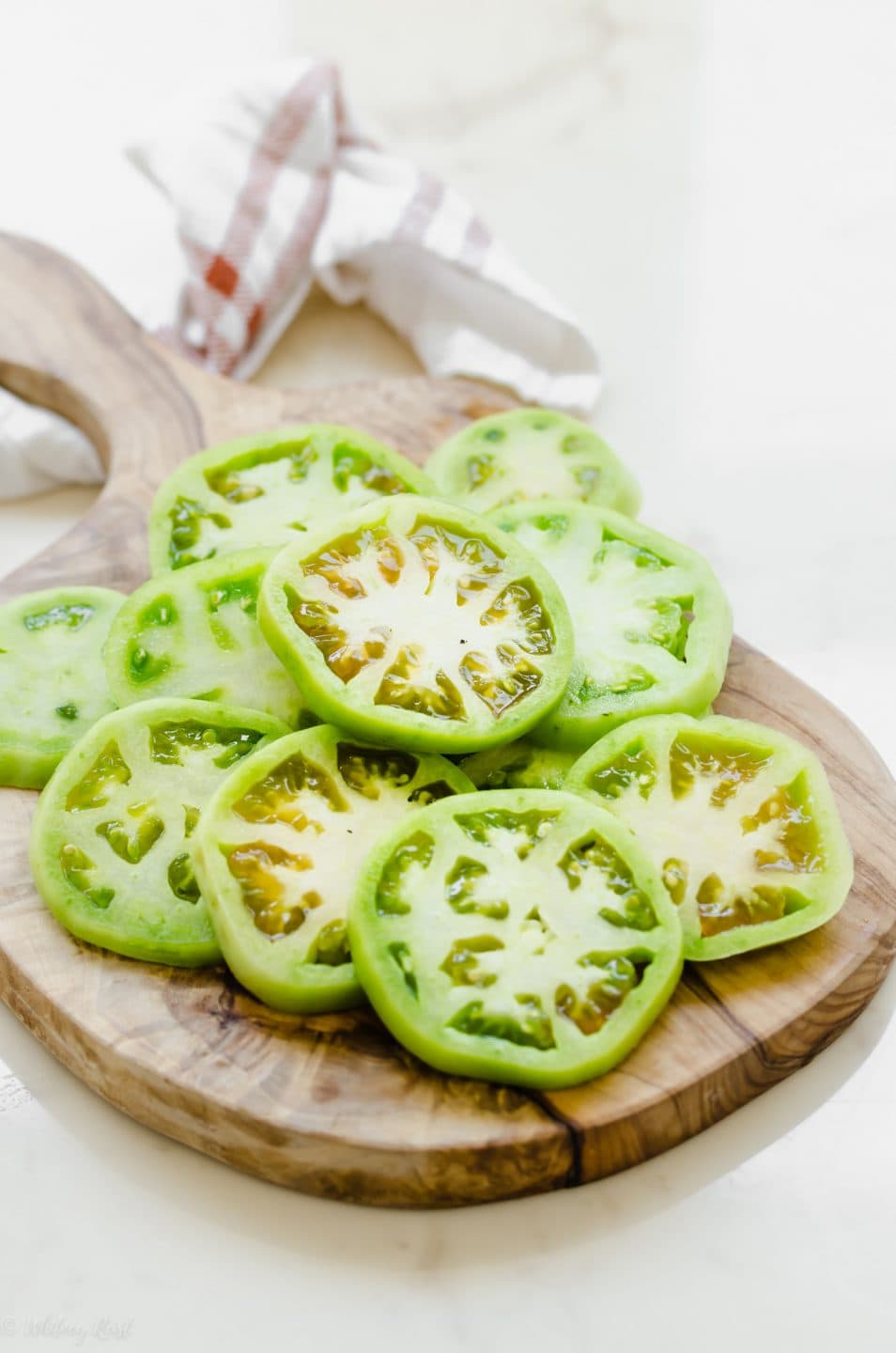 Sliced fresh green tomatoes on a olive wood cutting board.