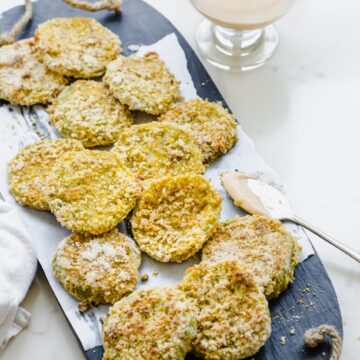 A slate platter lined with parchement paper and topped with oven-fried green tomatoes and a bowl of hot sauce aioli on the side.