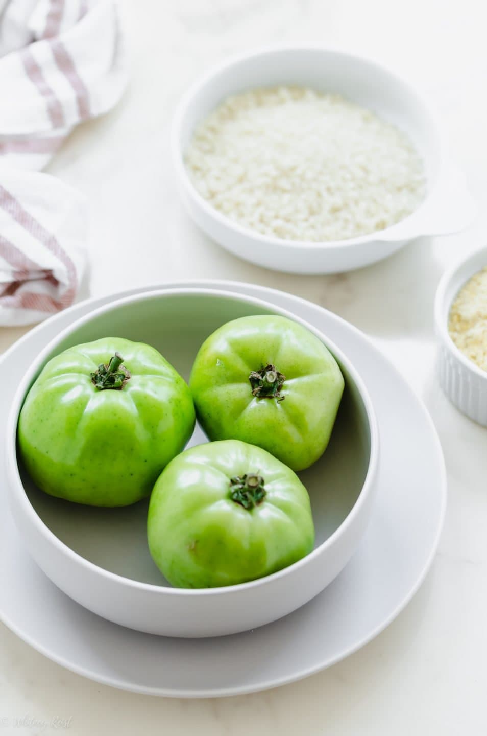 A white ceramic bowl filled with fresh green tomatoes and a bowl of Panko bread crumbs on the side.