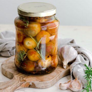 A large jar filled with pickled cherry tomatoes sitting on a cutting board.