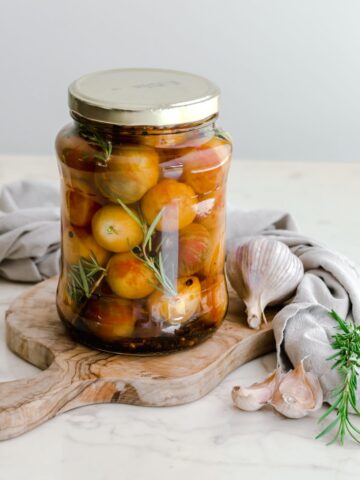 A large jar filled with pickled cherry tomatoes sitting on a cutting board.