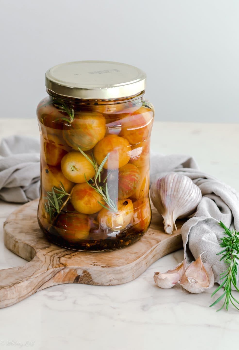 A large jar filled with pickled cherry tomatoes sitting on a cutting board.