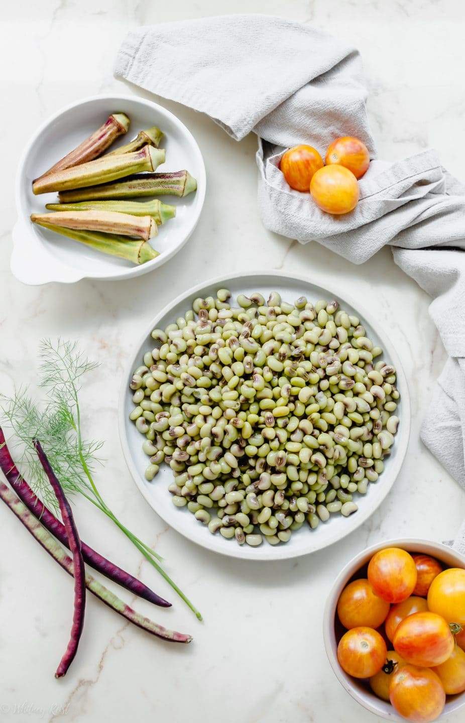 A plate of fresh purple hull peas with dishes of pickled okra, tomatoes, and purple hull peas on the side.