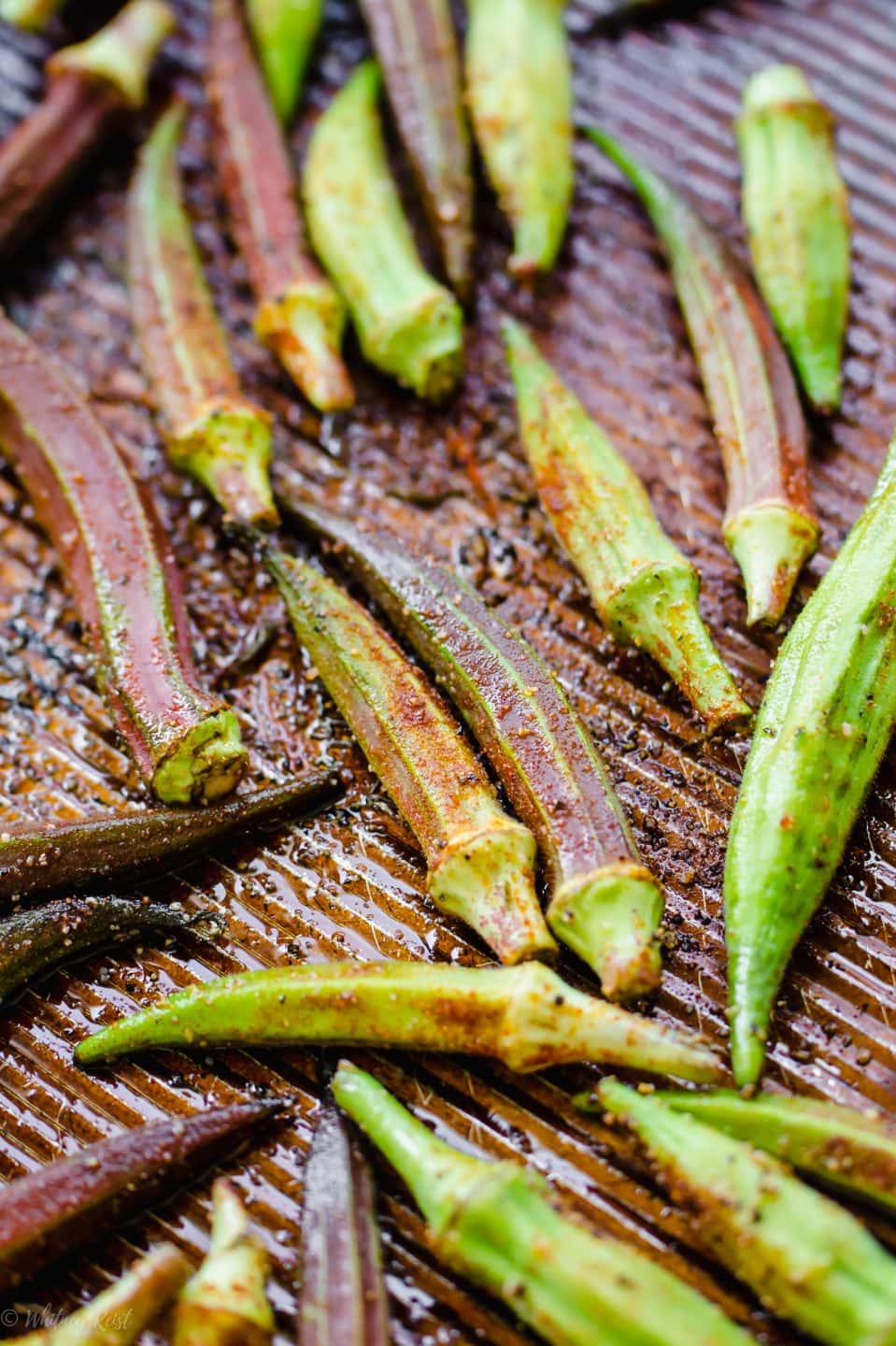 A baking sheet with raw okra pods and seasoning on top for roasting.