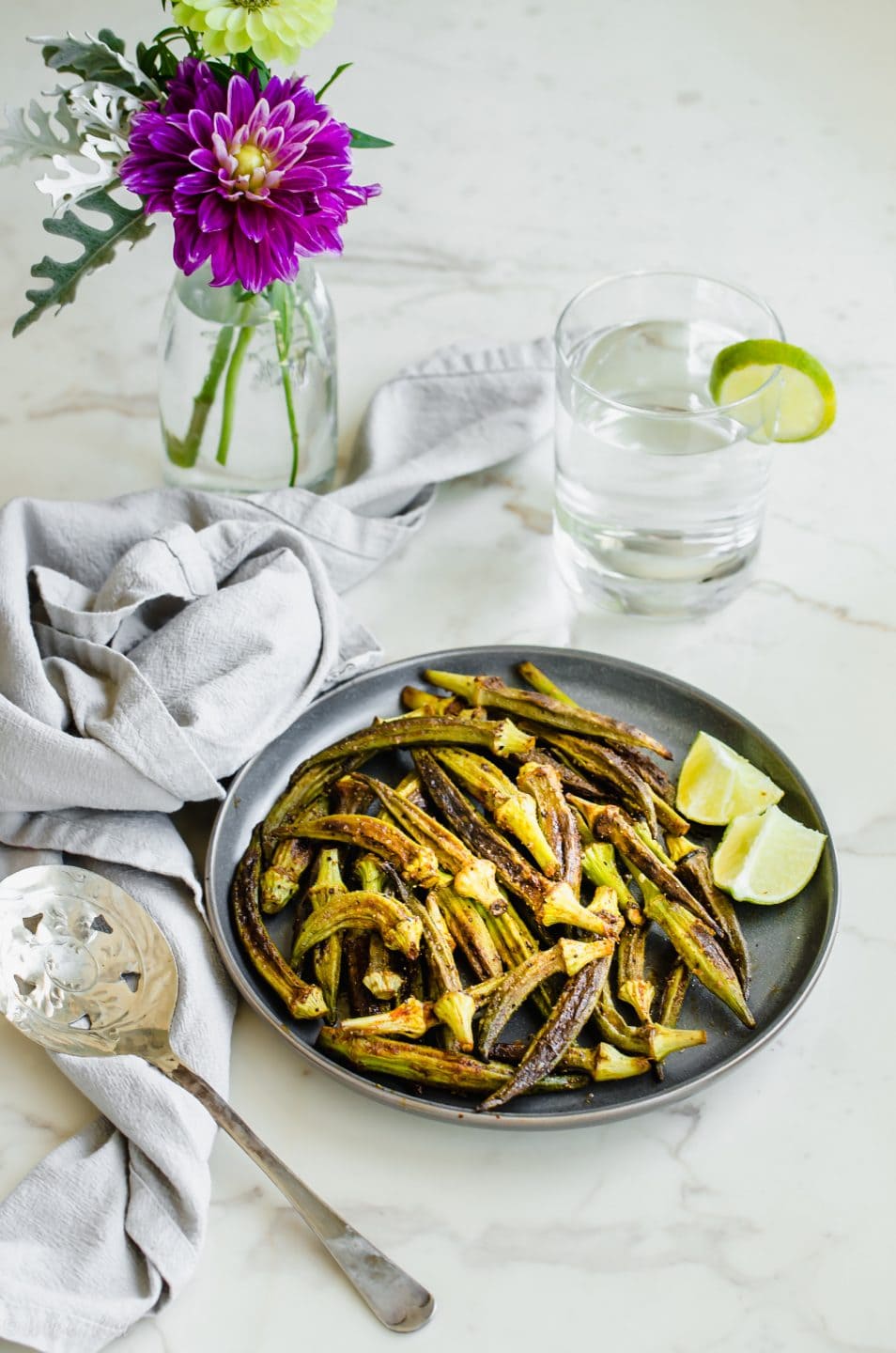 A gray plate with roasted okra and some fresh lime wedges on a white counter top.