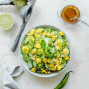 A grey bowl with Thai cucumber mango salad with a small dish of vinaigrette and fresh limes on the side.
