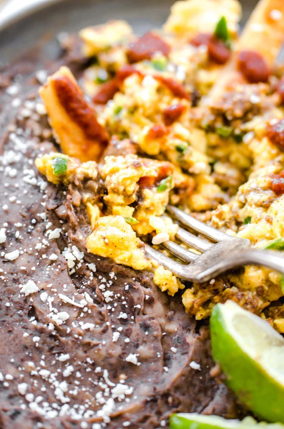 A fork digging into a plate of migas with refried black beans on the side. 