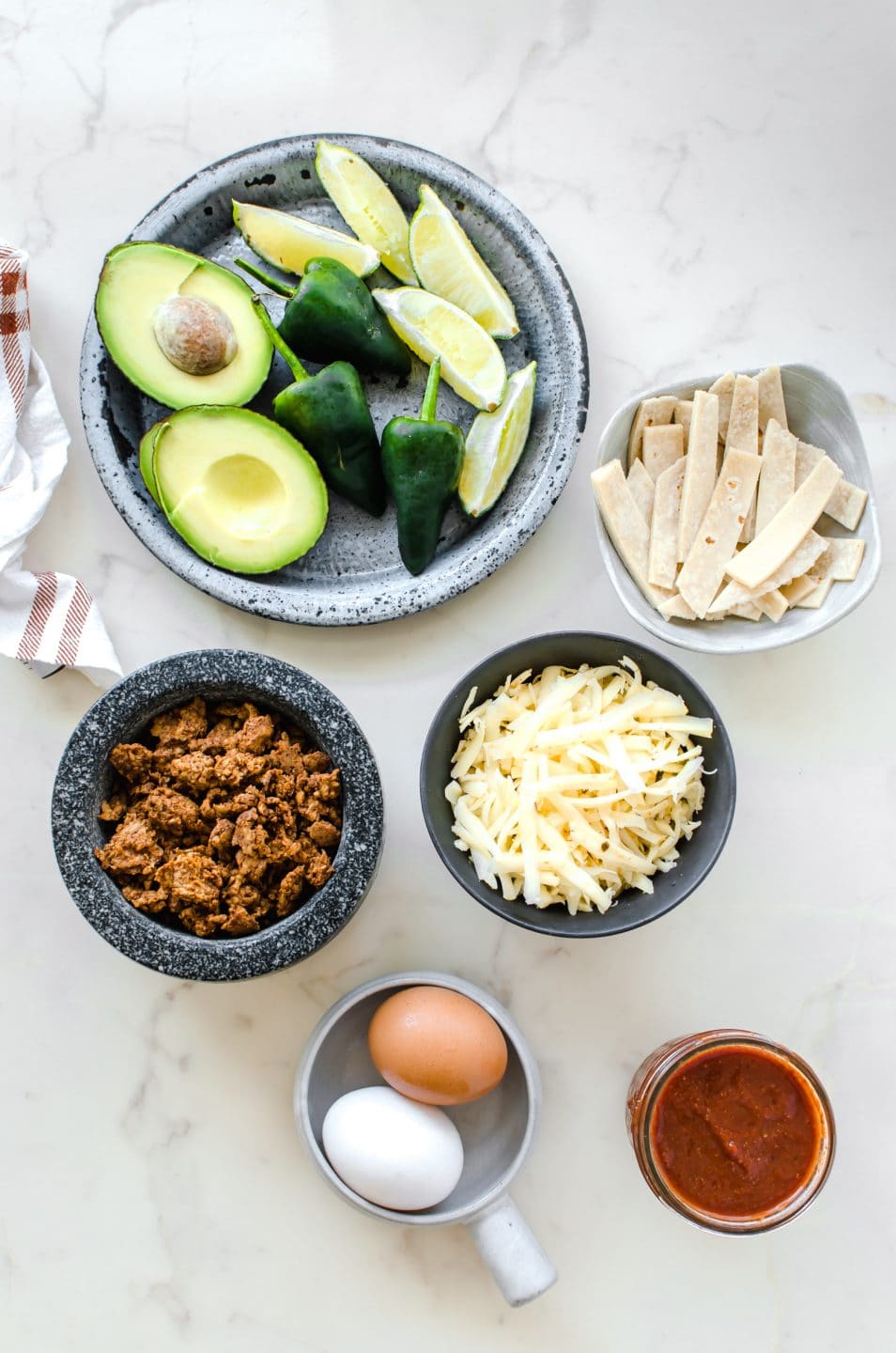 Various bowls filled with ingredients for making migas on a white matble counter. 