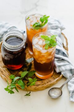 Two glasses of iced tea garnished with mint on a rattan wicker serving tray.