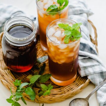 Two glasses of iced tea garnished with mint on a rattan wicker serving tray.