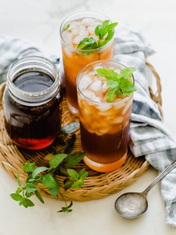 Two glasses of iced tea garnished with mint on a rattan wicker serving tray.
