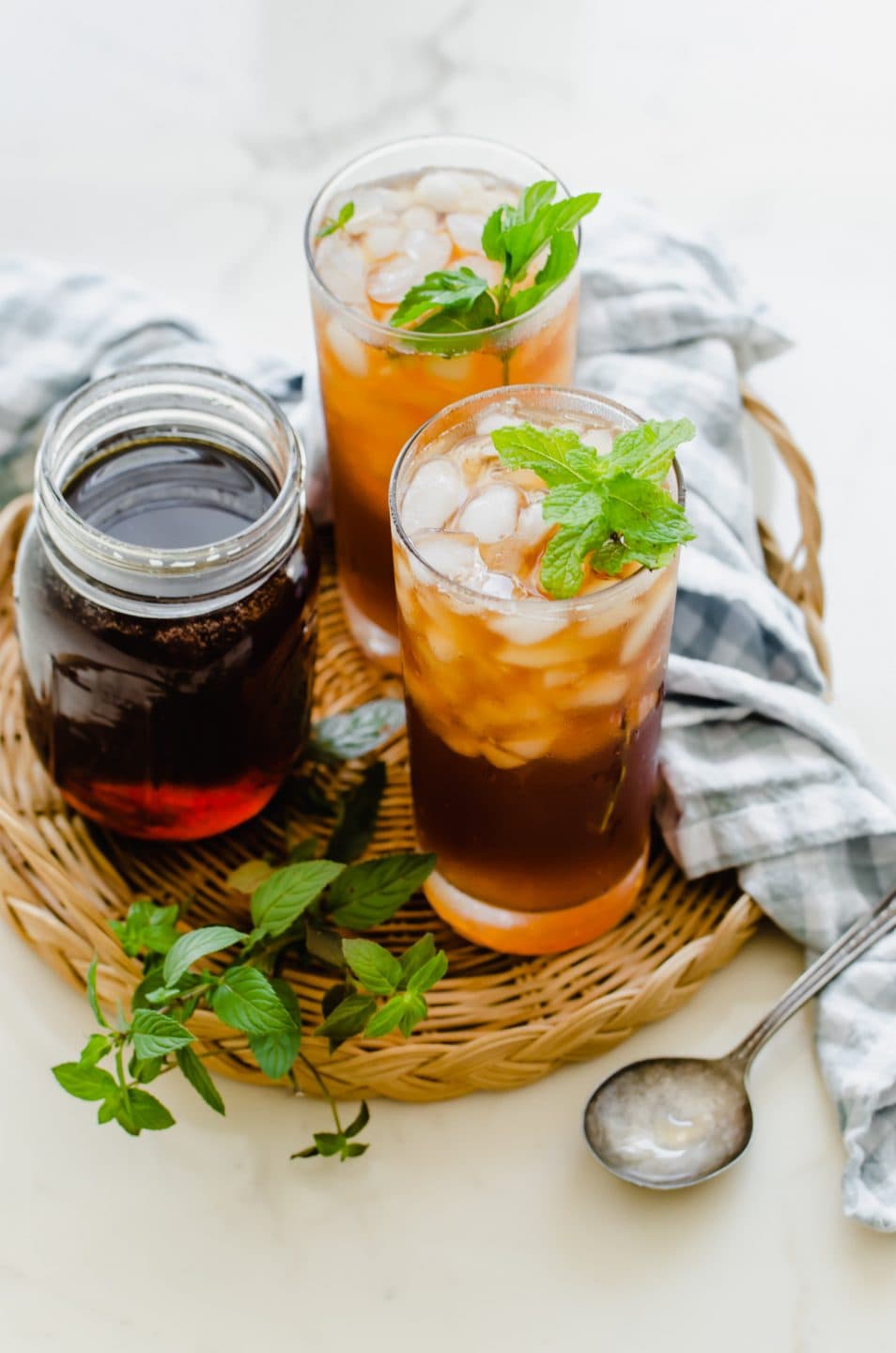 Two glasses of iced tea garnished with mint on a rattan wicker serving tray.