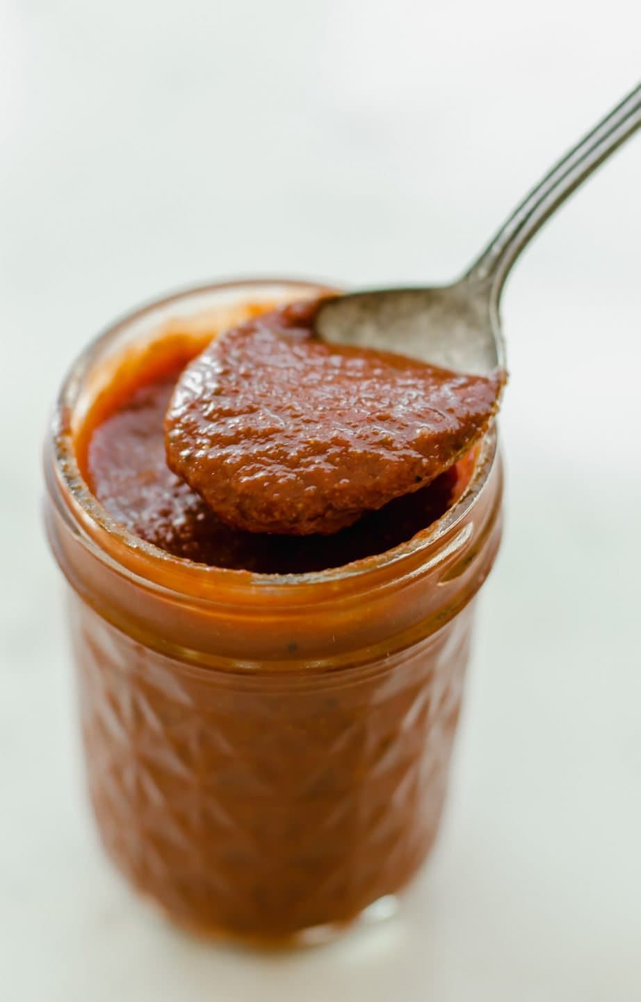 A jar of homemade taco sauce with a spoon lifting some out of the jar.