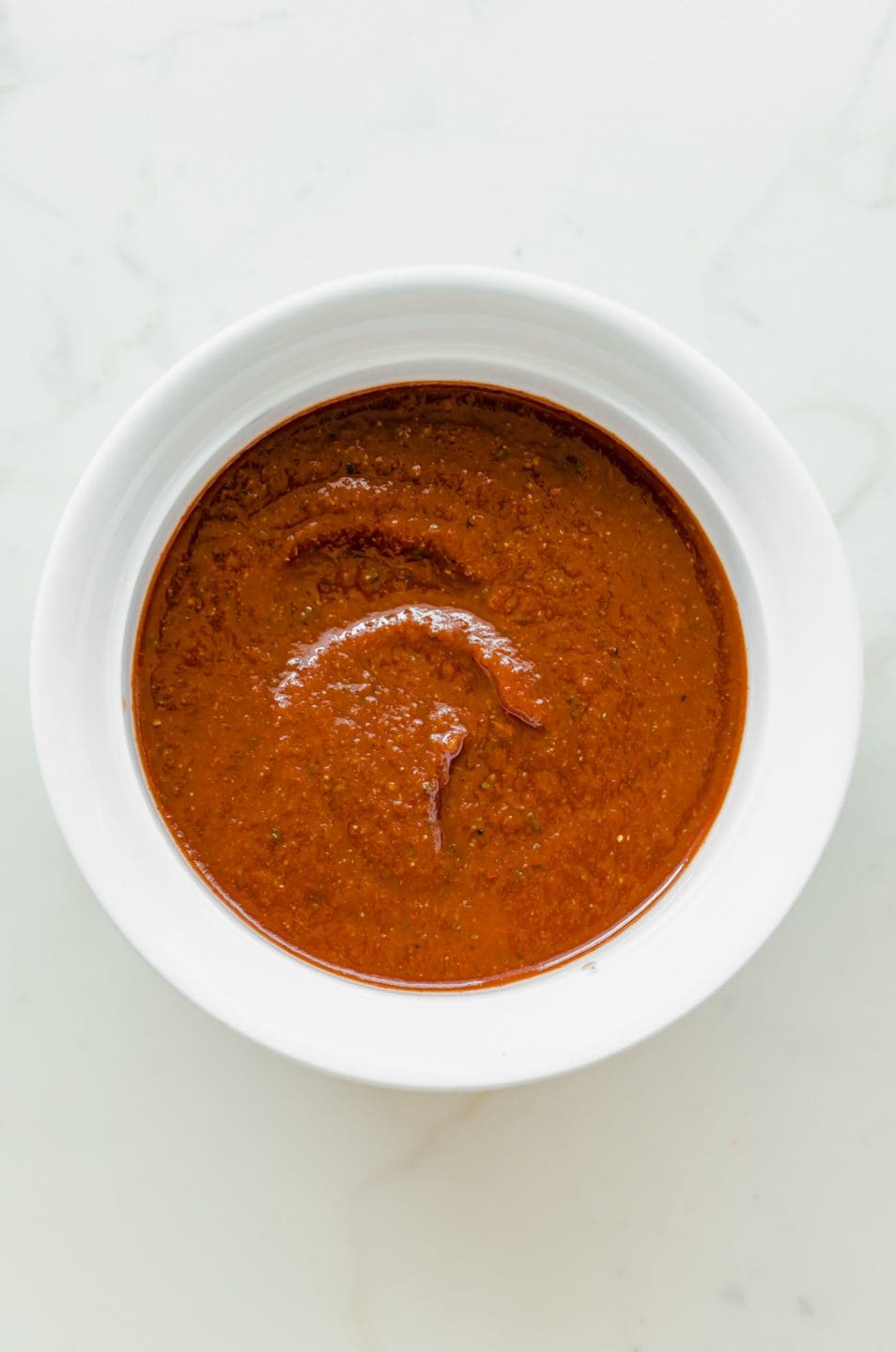 Overhead shot of a while bowl filled with easy homemade taco sauce on a marble surface.