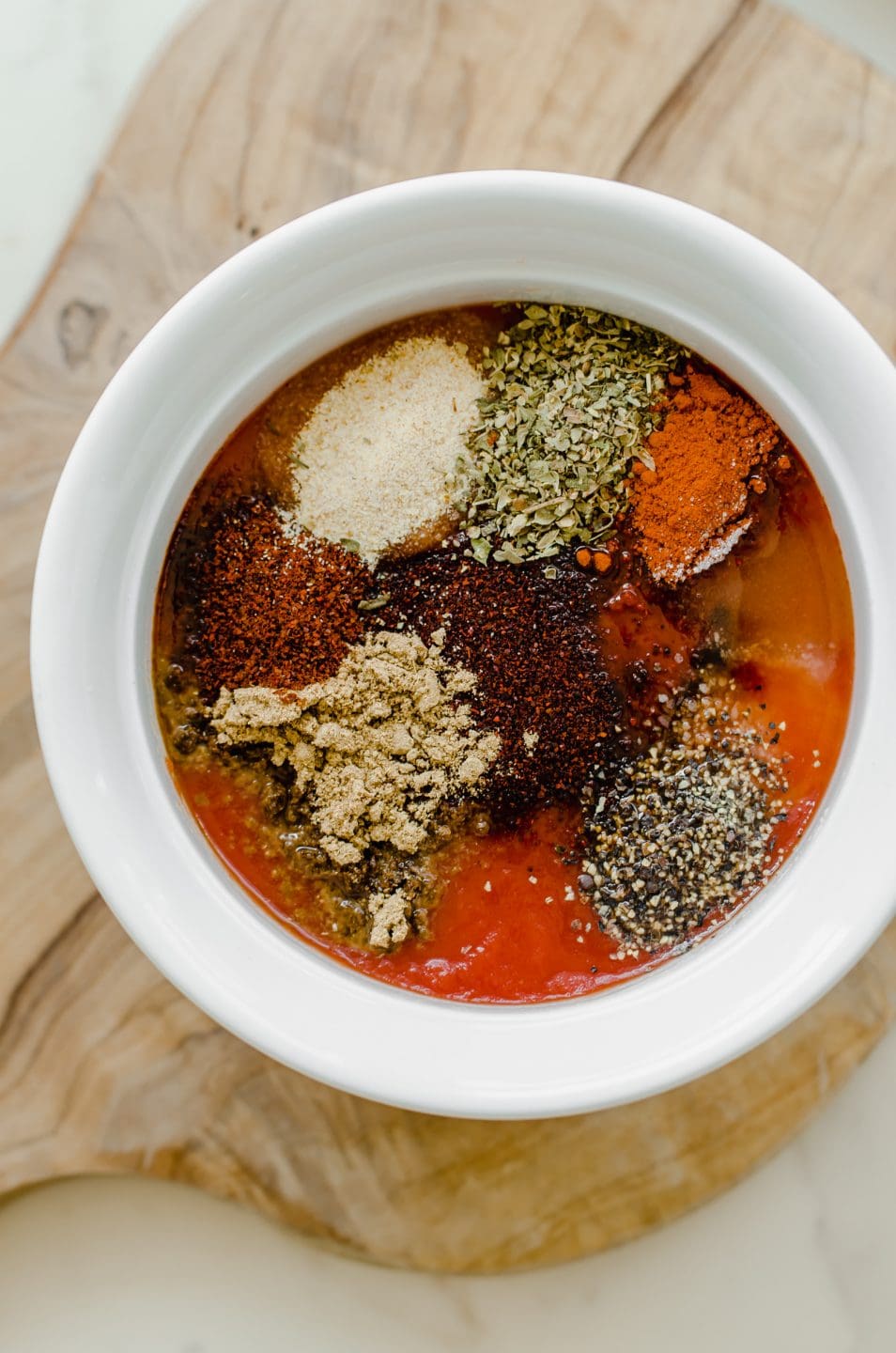 All of the spices for homemade taco sauce in a white bowl sitting on a wood board. 