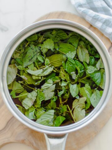 A bunch of fresh chopped mint in a saucepan filled with simple syrup.