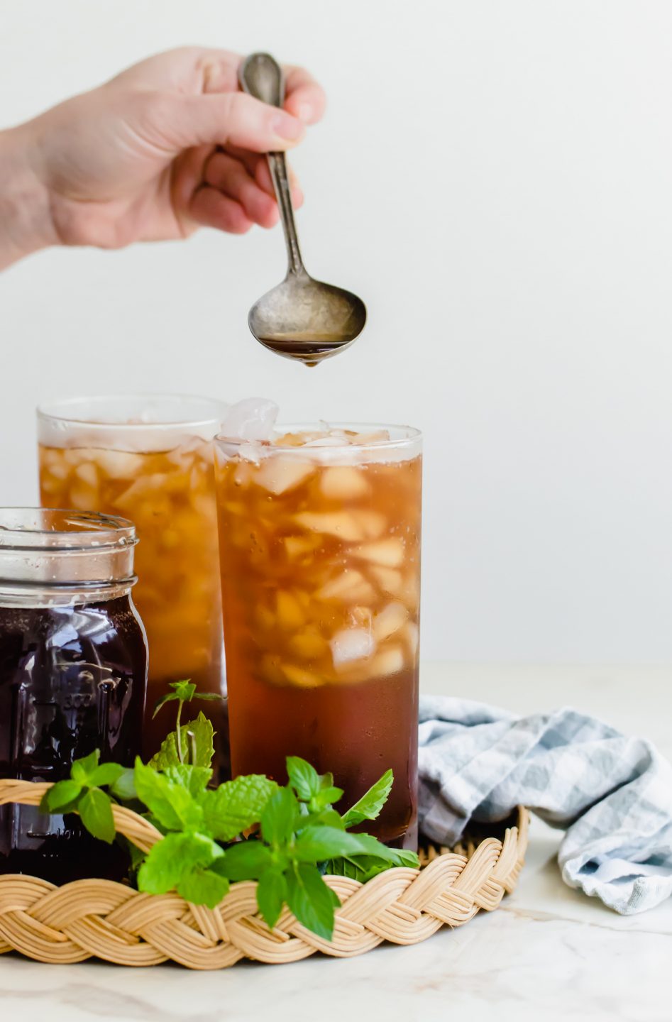 A hand spooning simple syrup into a full glass of iced tea.