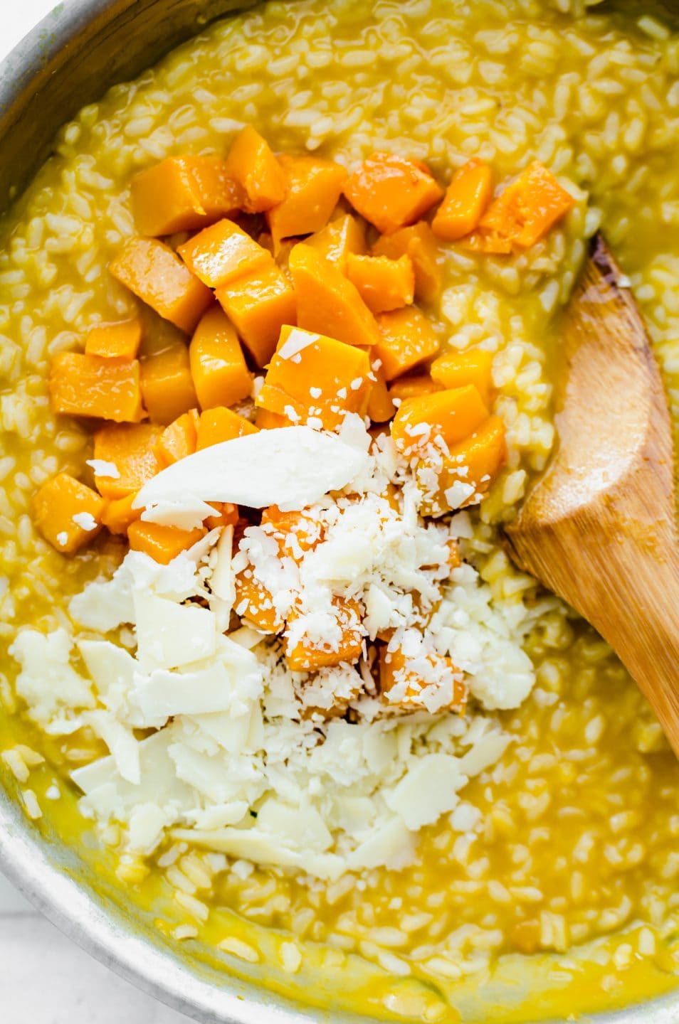 A spoon stirring roasted butternut squash and Parmesan cheese into a skillet of risotto.