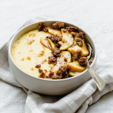 A white bowl filled with grits and cinnamon apples sitting on a taupe and cream gingham napkin.