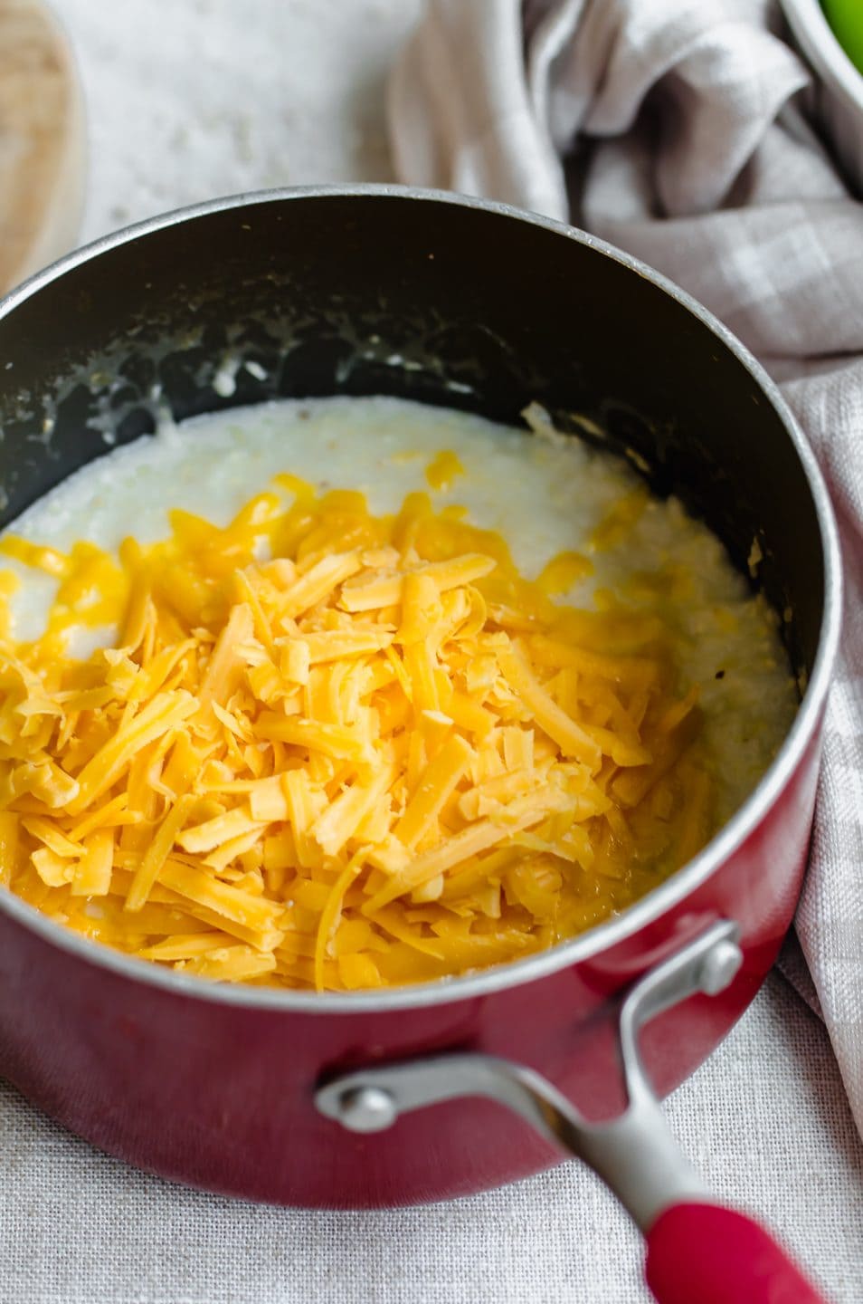 A saucepan with cooked grits topped with cheddar cheese that is about to be stirred in.
