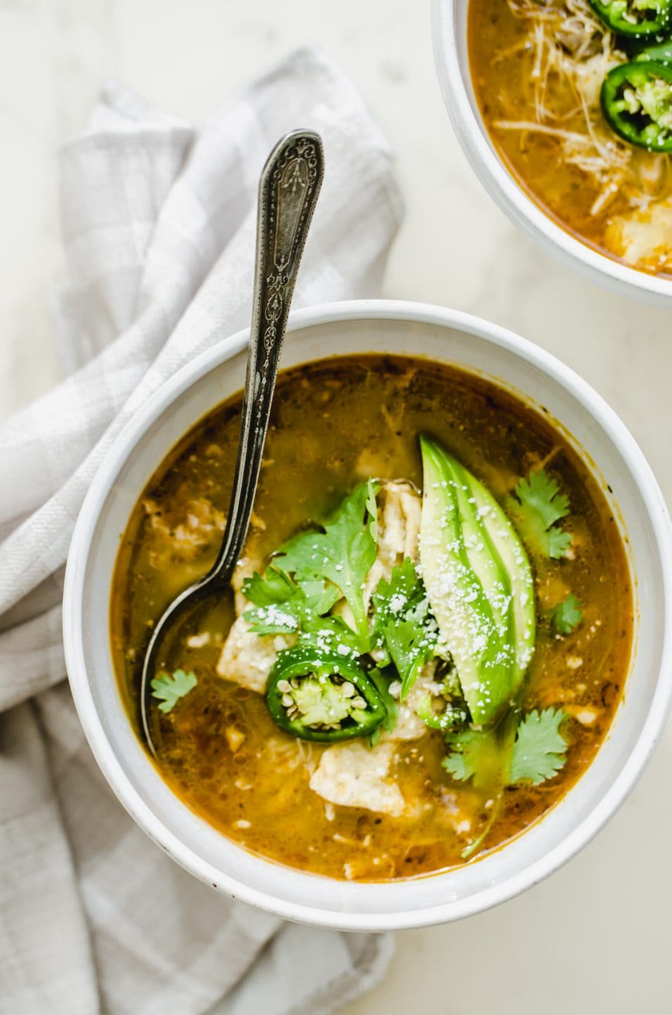 A white bowl of soup filled with posole verde and garnished with avocado and cilantro.