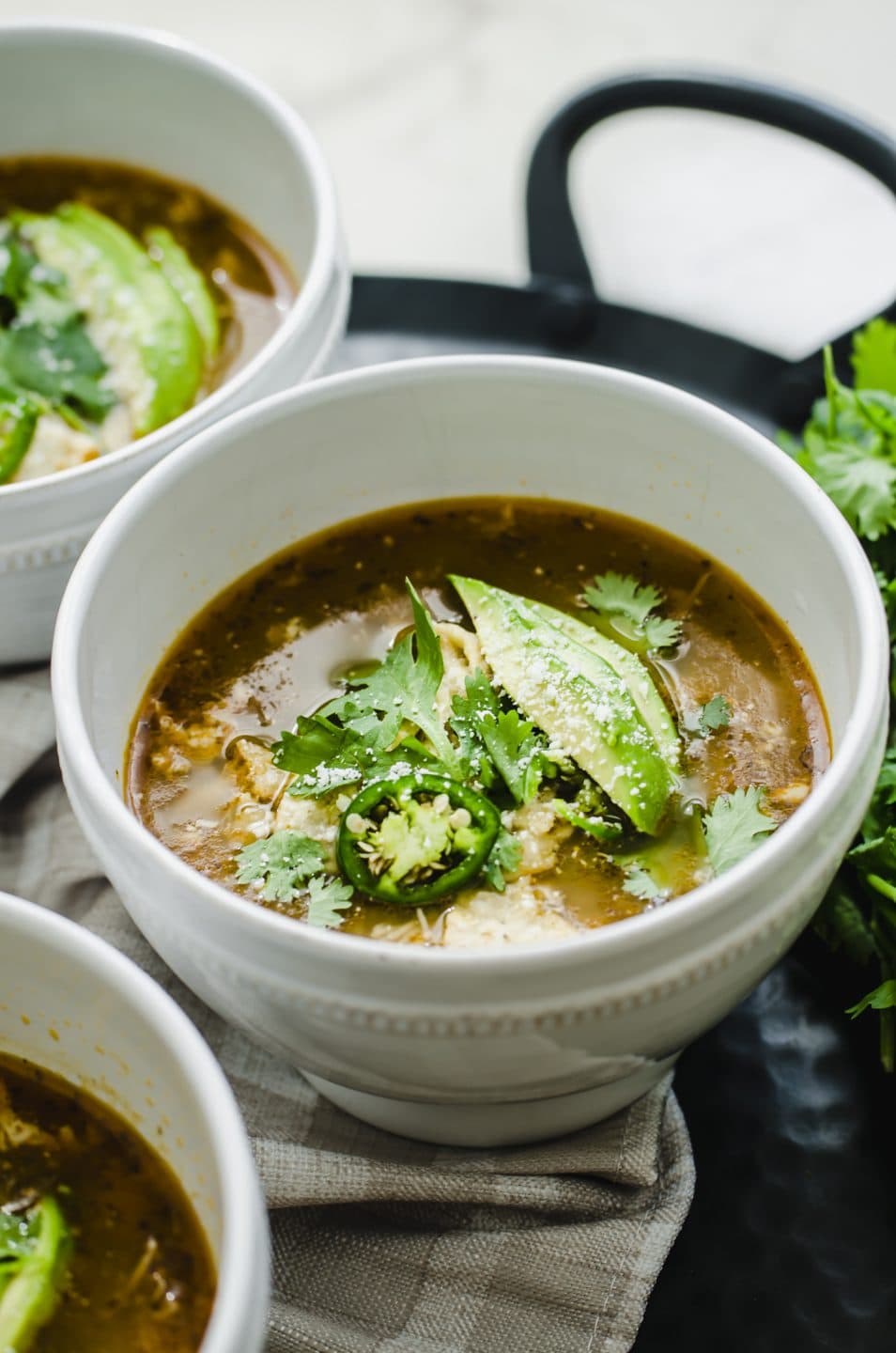 A white bowl of soup filled with posole verde and garnished with avocado and cilantro.