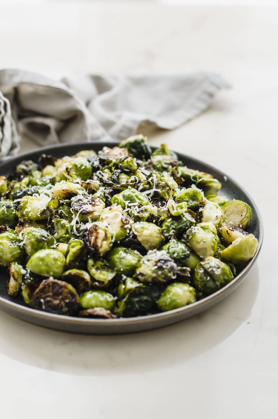 A grey plate filled with crispy roasted brussels sprouts on a marble countertop.