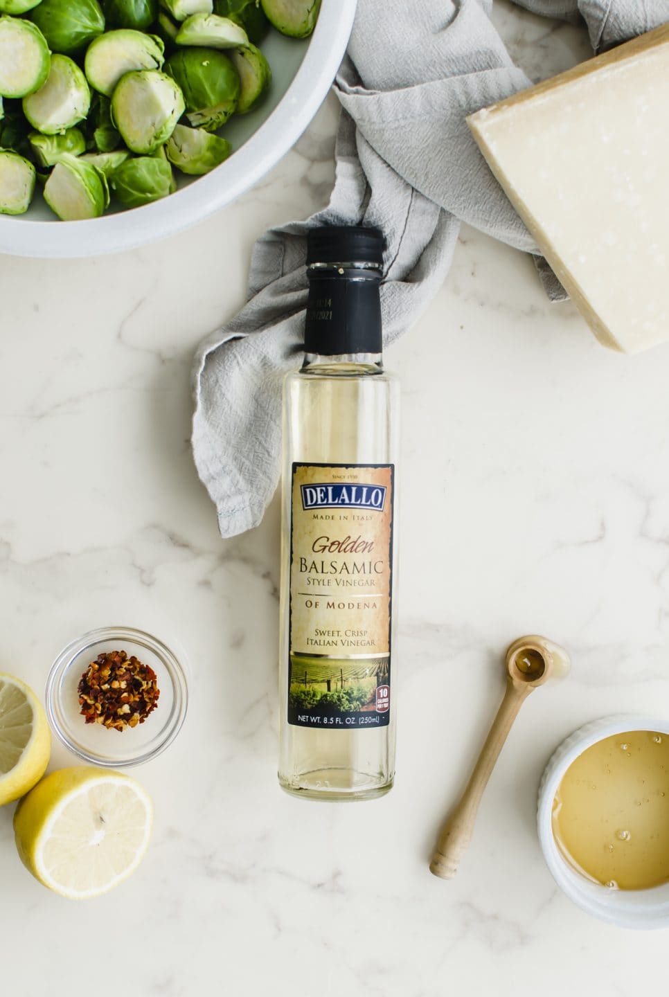 A bottle of white balsamic vinegar surrounded by prep bowls with other ingredients.