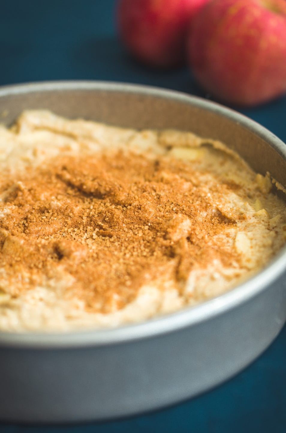 A cake pan filled with apple cake batter and topped with cinnamon sugar.