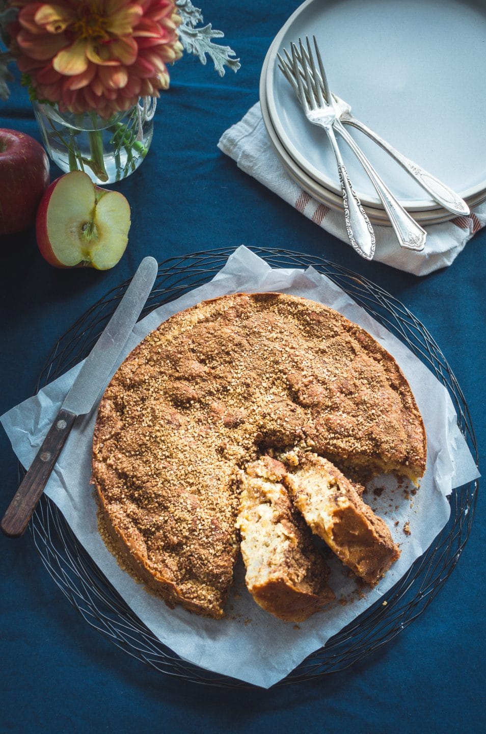 An overhead shot of an apple cake on a wire rack with two pieces sliced out of the cake and ready to serve.