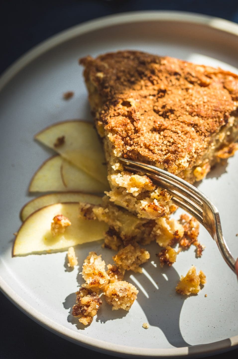 A fork slicing a bite out of a piece of cinnamon apple cake on a plate.