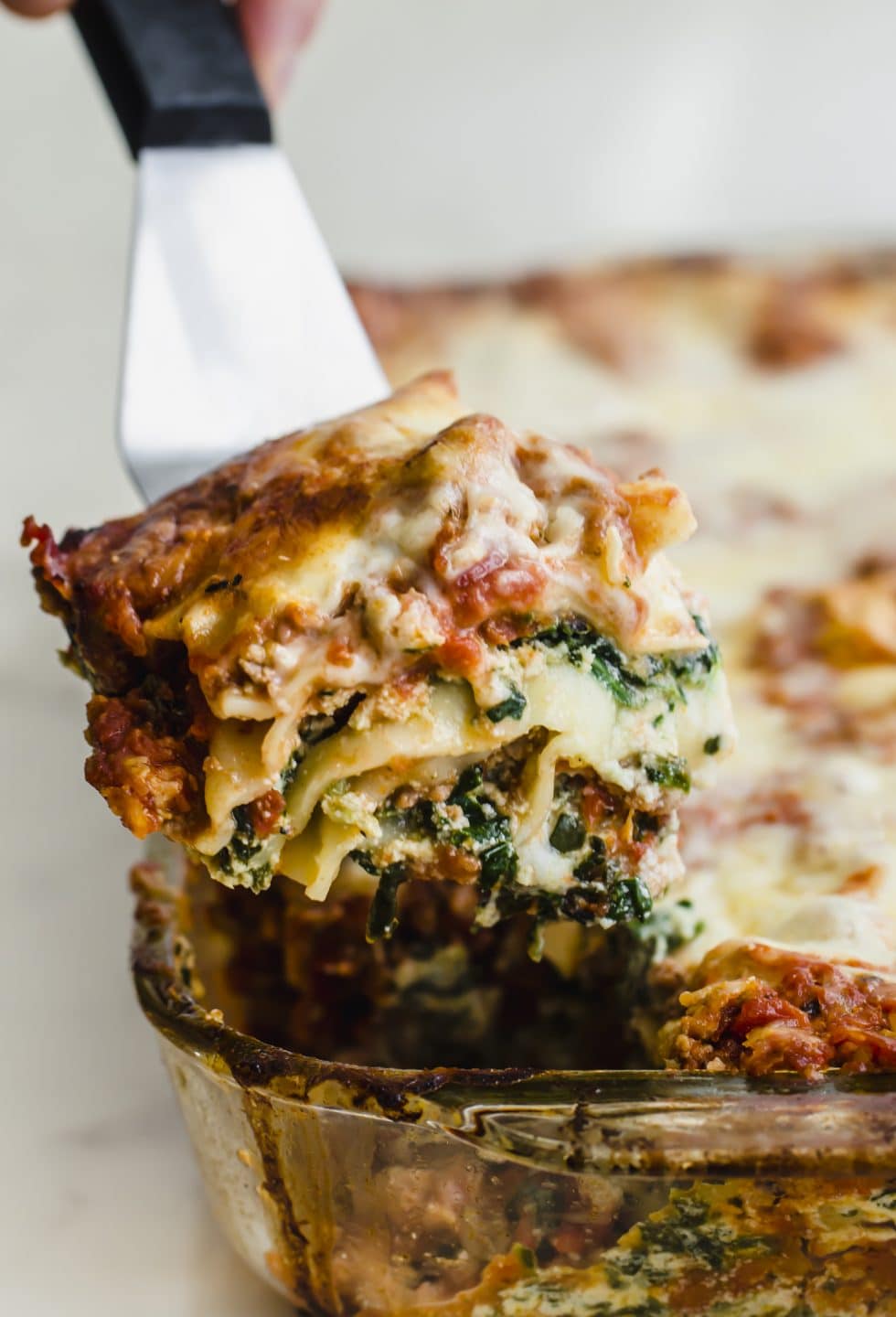 A spatula lifting a squash of lasagna out of a baking dish.