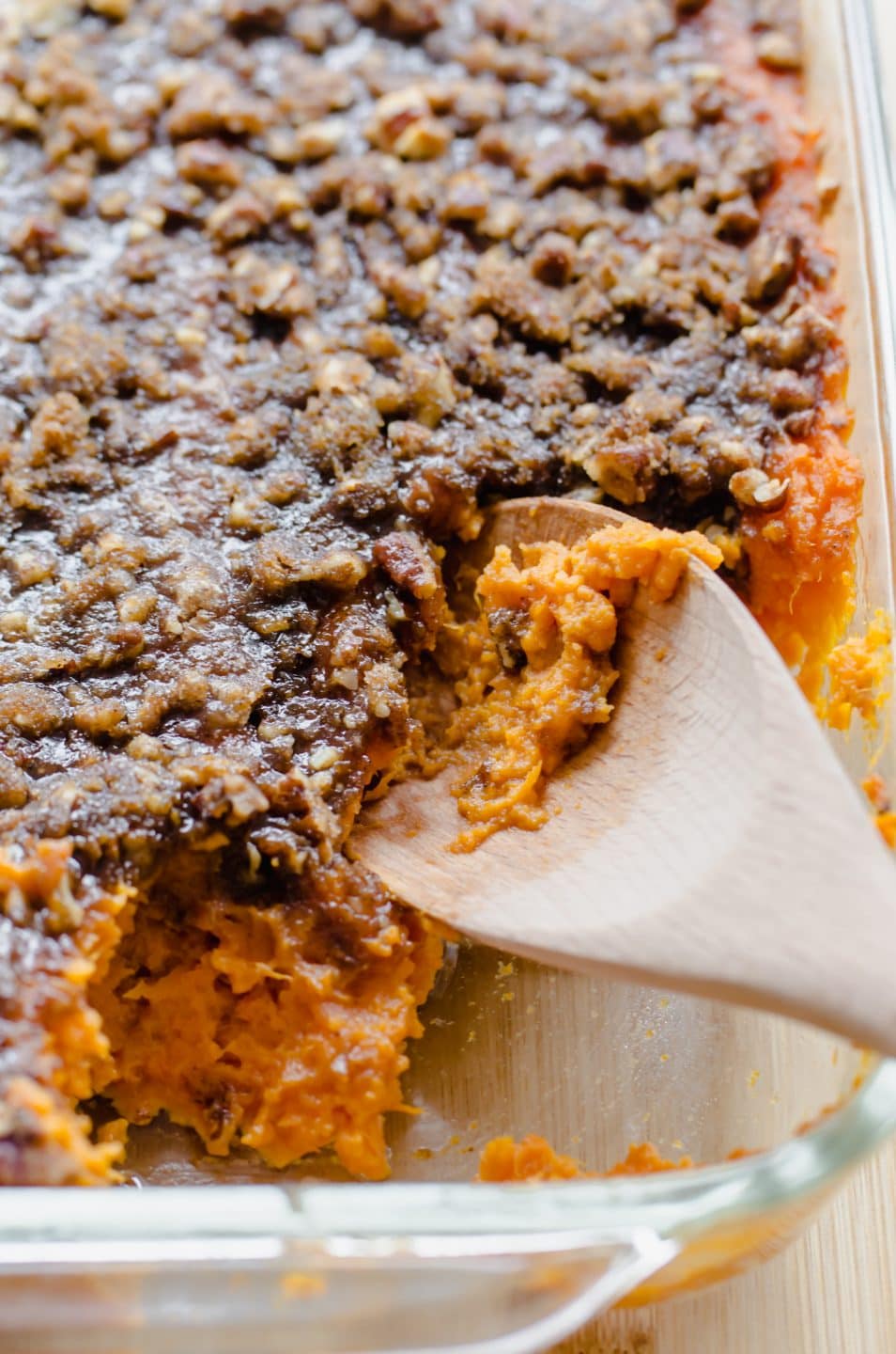 A close-up shot with a wooden spoon digging into a sweet potato casserole. 