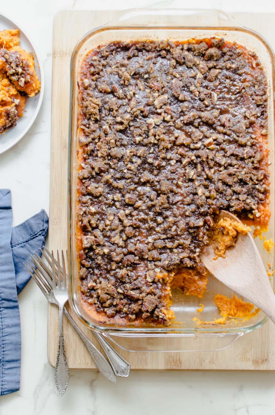 An overhead shot of a dish of Apple Cider Sweet Potato Casserole on a cutting board with a blue napkin on the side.