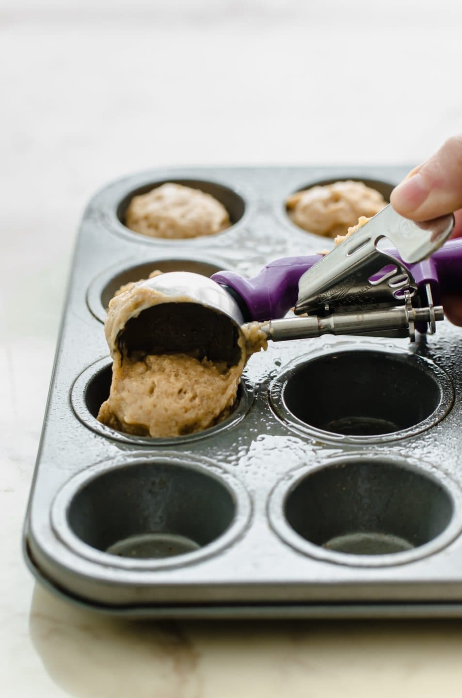 A cookie dough scoop placing batter into a mini muffin tin.