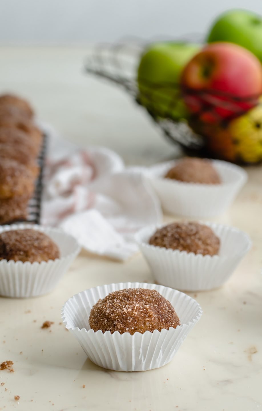 Baked apple cider donut holes in white paper muffin cups on a counter top.
