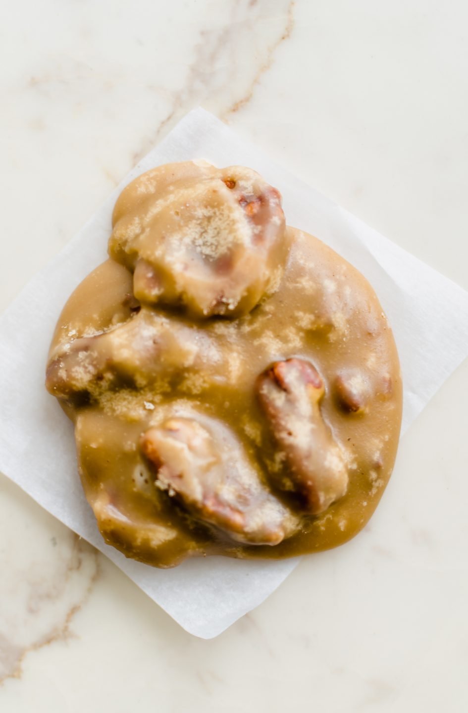 A piece of pecan praline candy on a piece of parchment paper.