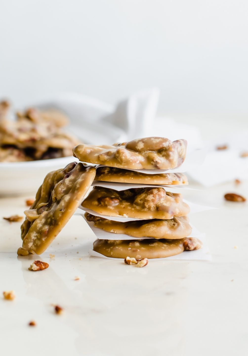 A stack of boiled cider pecan pralines stacked with squares of parchment paper.