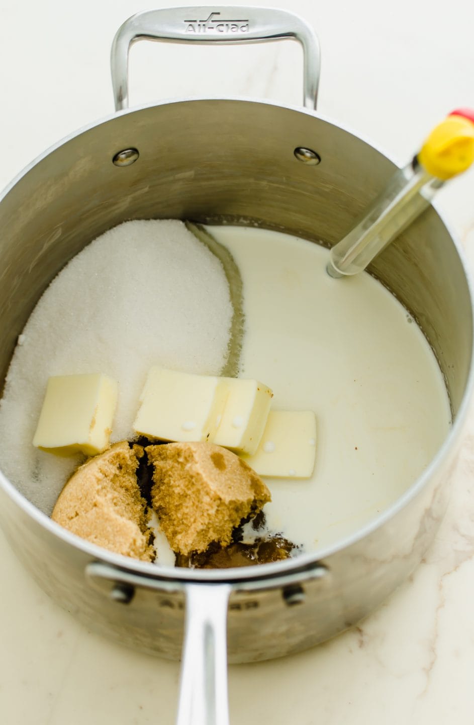 A metal pot filled with ingredients for making pecan pralines and a candy thermometer inserted.