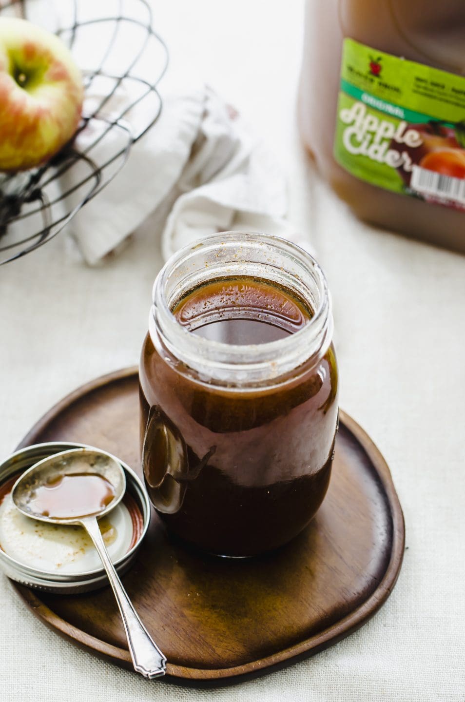 A jar of boiled apple cider syrup sitting on a wooden plate with a small spoon on the side.