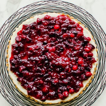 An overhead shot of a cranberry cheesecake tart on a black wire charger.