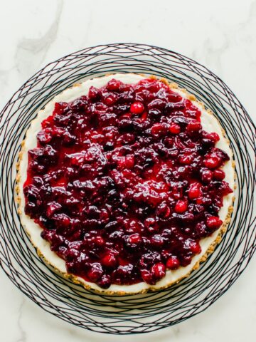 An overhead shot of a cranberry cheesecake tart on a black wire charger.