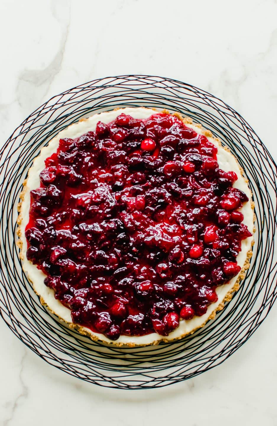 An overhead shot of a cranberry cheesecake tart on a black wire charger.