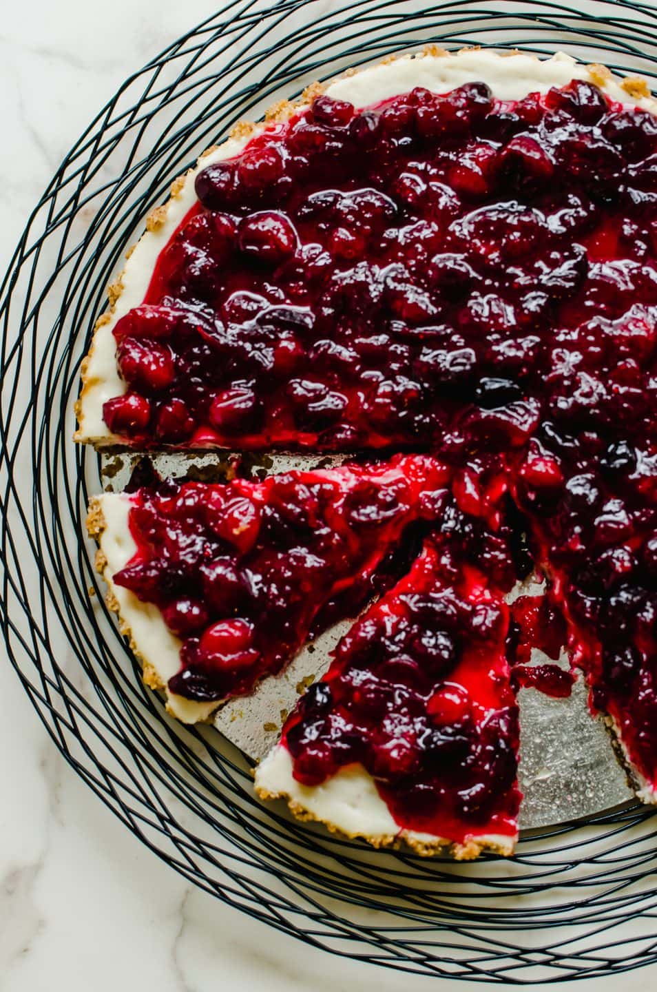 A close-up shot of a cranberry cheesecake tart with two slices being removed.