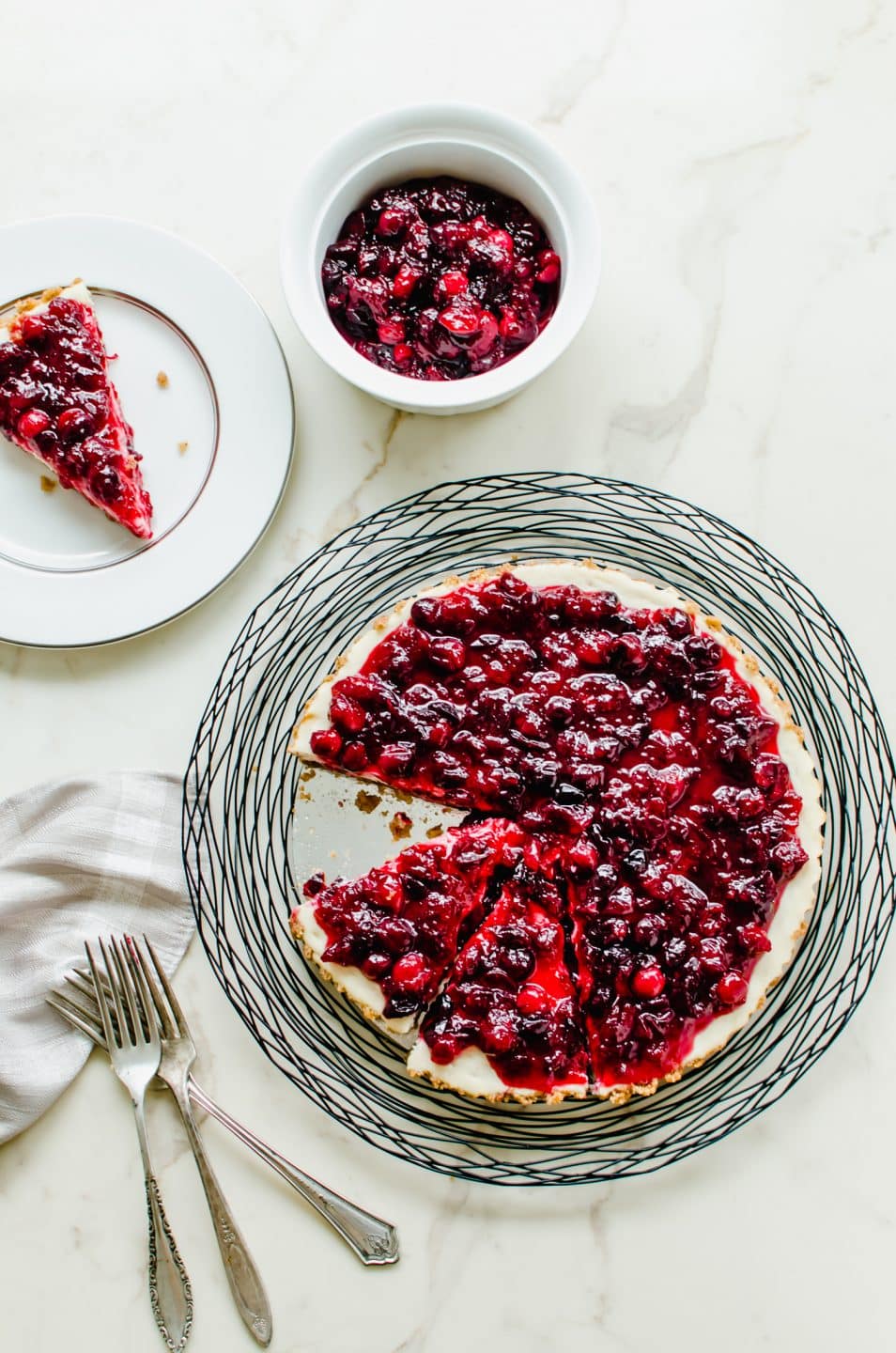 A cranberry cheesecake tart on a wire charger with a slice of tart on a plate to the side.