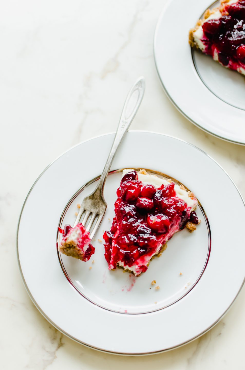 A slice of cranberry cheesecake tart on a silver-rimmed china plate with a bite on an antique fork.