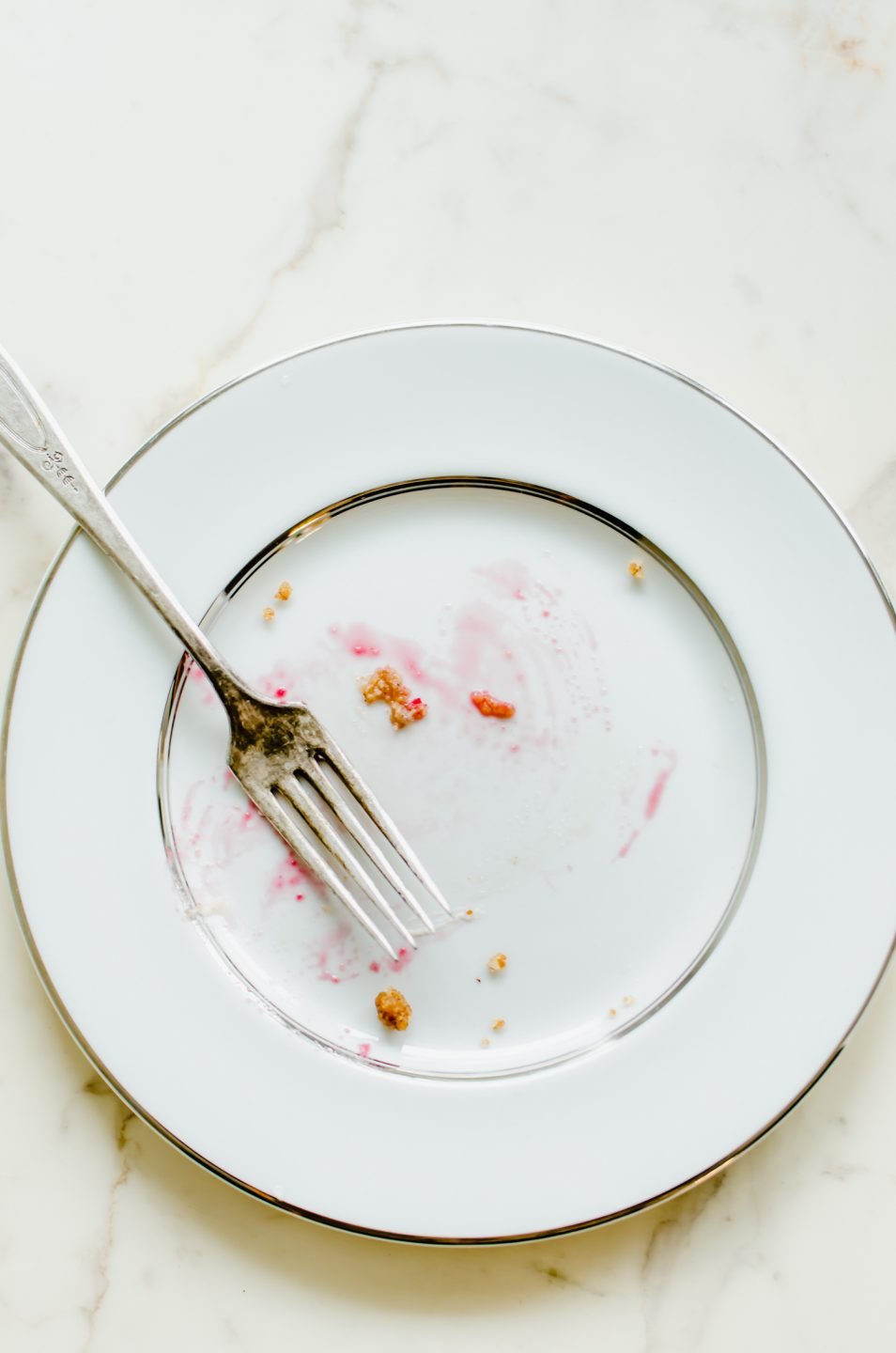 An empty china plate with smears of cranberry cheesecake tart and a fork.