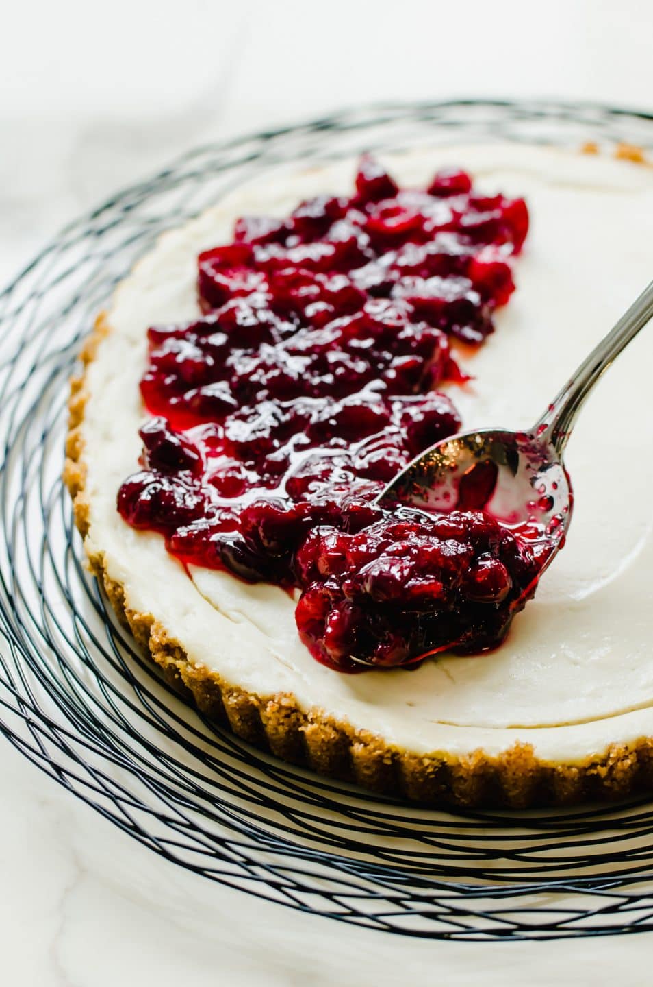 Cranberry topping being spooned onto a cheesecake tart.